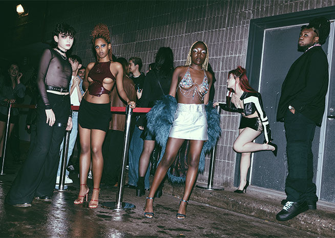 Fashion-forward individuals in eclectic outfits queue outside a club at night.