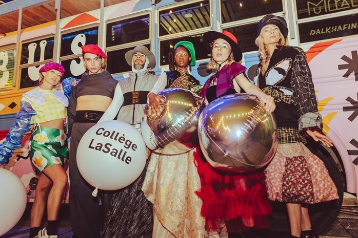 Group of models showcasing diverse fashion styles, posing with balloons in front of a streetcar.