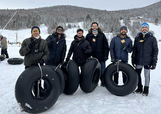 Six friends stand with snow tubes at a snowy resort, ready for winter fun.