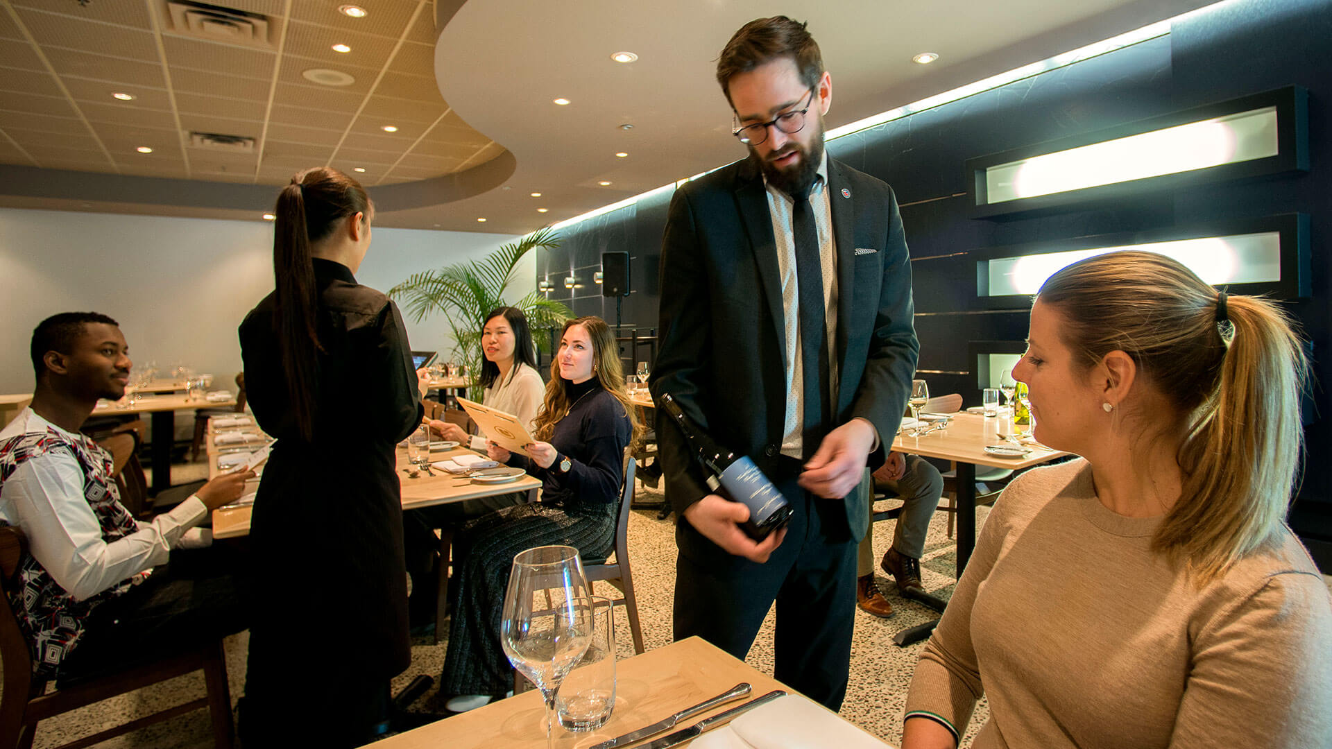 A waiter attending to guests at a college-run restaurant, enhancing the educational ambiance with practical service experience.