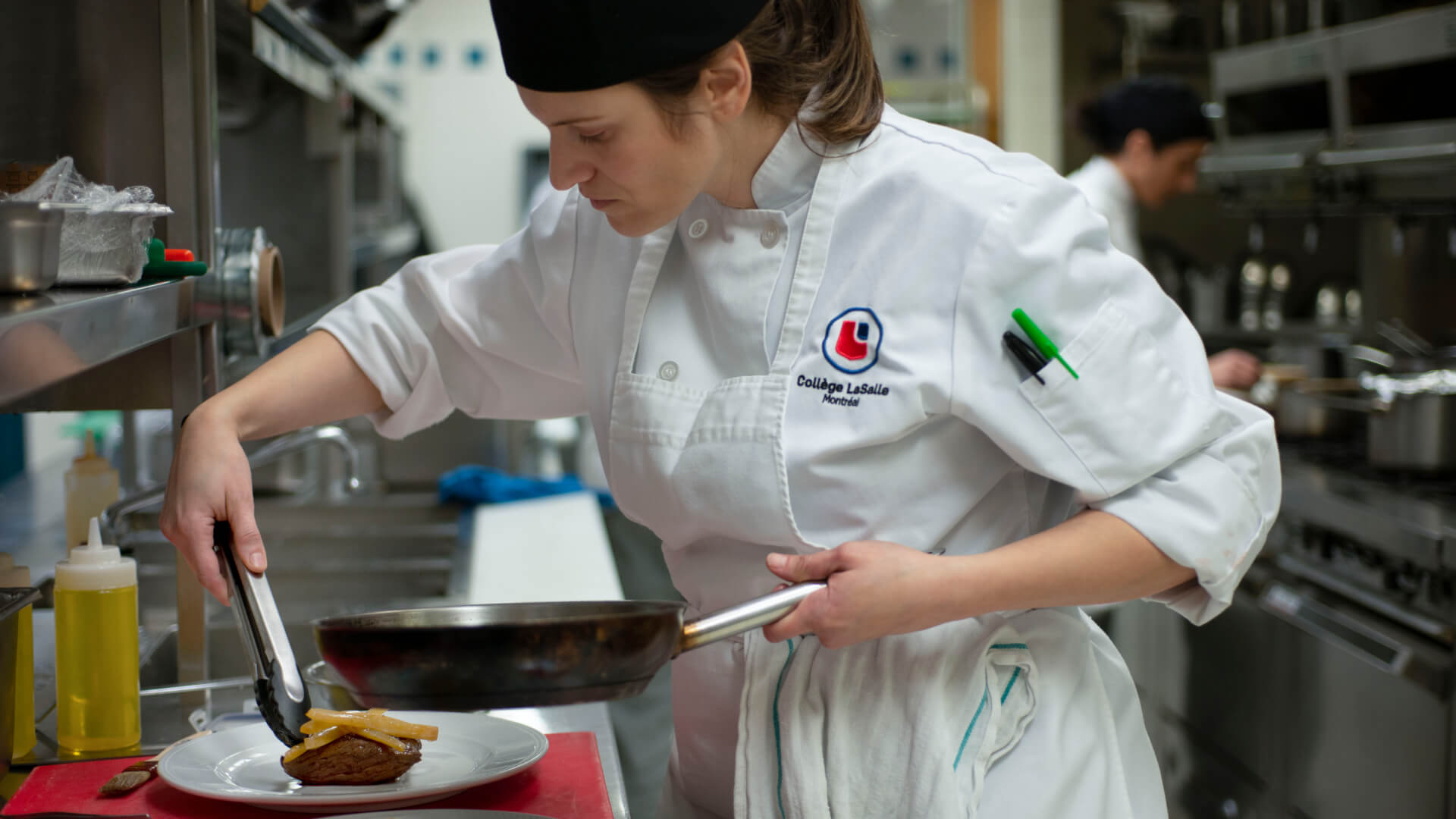 A dedicated culinary student at LaSalle College expertly plates a dish, focused on detail in a bustling kitchen.