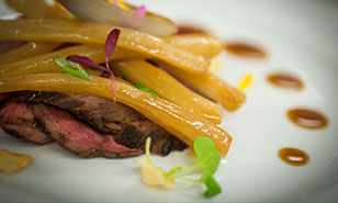 Sliced beef topped with glazed carrots, elegantly plated with artistic sauce accents.