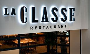 Illuminated signage for "La Classe Restaurant" with a cozy dining area visible in the background.