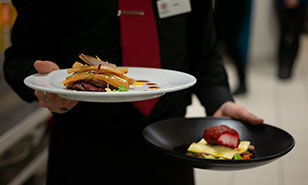  A waiter presenting two sophisticated dishes, showcasing fine dining plating techniques.