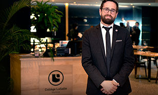 A professional host in a formal suit stands confidently in the elegant setting of a restaurant associated with College LaSalle.