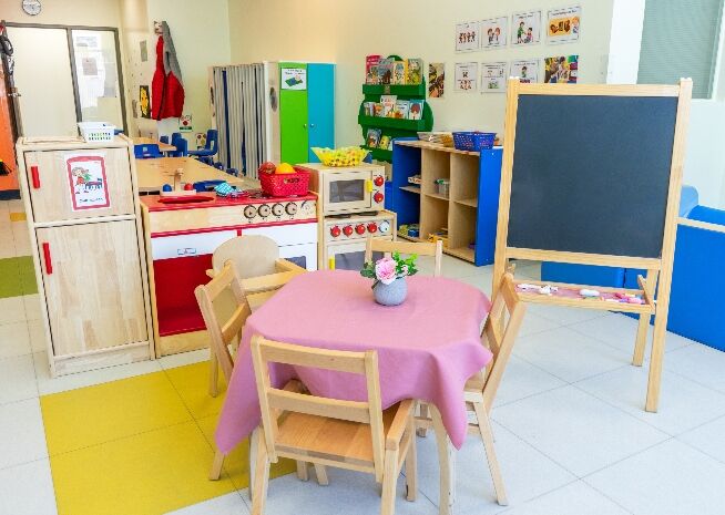 Salle de maternelle vivante avec jouets éducatifs colorés, meubles à taille enfant et tableau noir pour un apprentissage ludique.