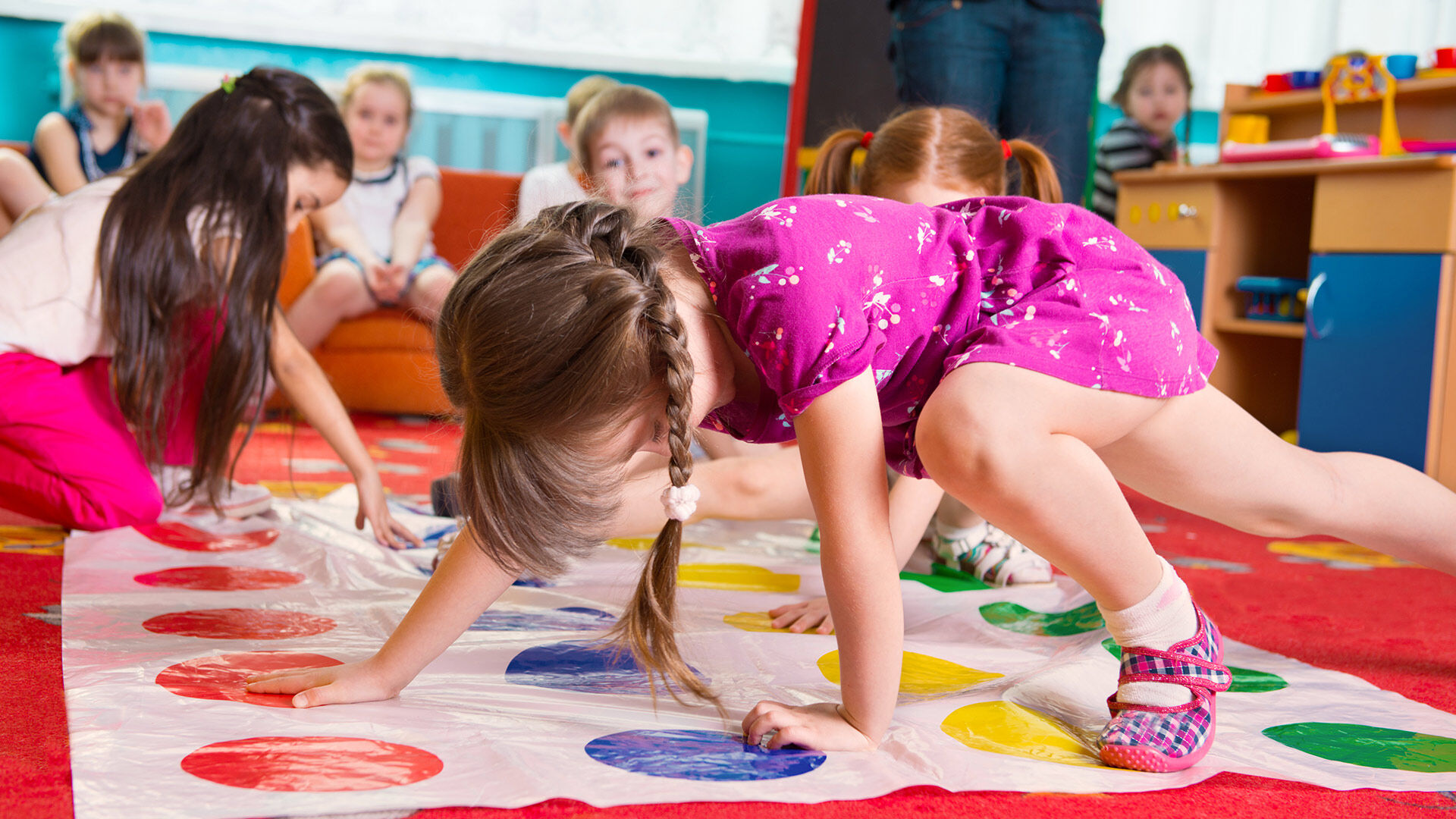 Des enfants jouent au Twister dans une salle de classe colorée, illustrant le mouvement et l'espièglerie.