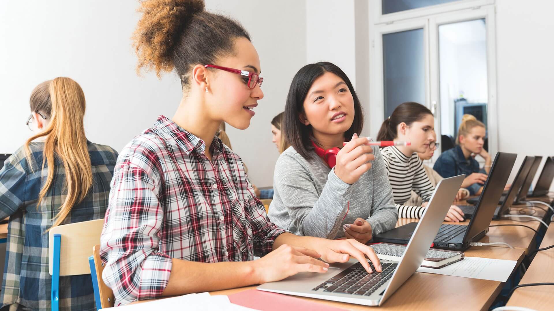 Étudiants engagés dans un apprentissage collaboratif avec des ordinateurs portables dans une salle de classe, discutant et partageant activement des idées.