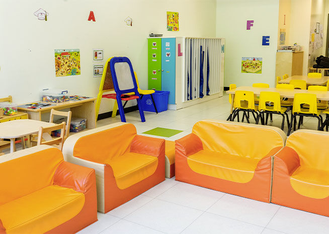 Une salle de maternelle vivante avec des tables jaunes, des canapés oranges et des jouets éducatifs, promouvant un espace d'apprentissage stimulant.