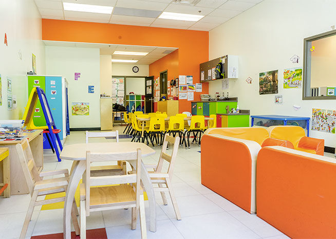 Une salle de classe de maternelle ordonnée dotée d'un ensemble de jeu de cuisine, d'un canapé bleu et de chaises bleues aux tables, prête pour des activités d'apprentissage.