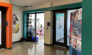 The entrance to a beauty school, featuring posters on glass doors and a glimpse of the stylish interior.