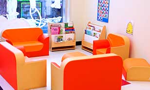 A cozy reading nook for children with orange and yellow chairs, bookshelves, and colorful decorations.