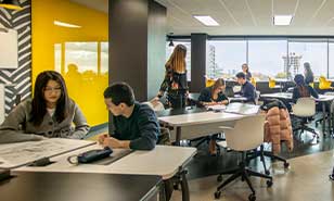 Students focused on their work in a brightly lit study space with yellow accent walls and modern furnishings.