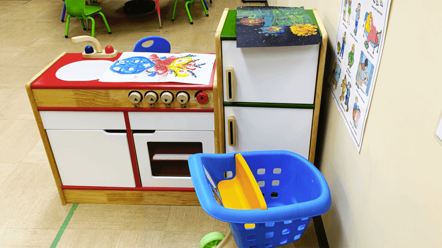 Toy kitchen setup in a classroom with colorful utensils, and children's artwork on the walls.