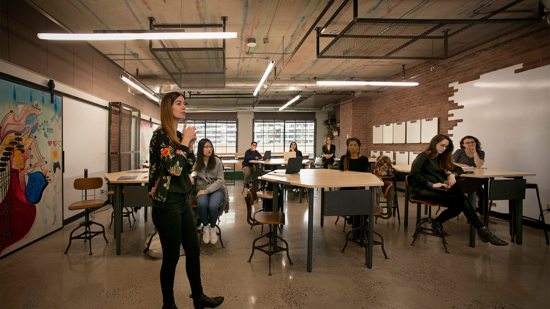 A presenter addresses a diverse group of attentive participants in an urban loft-style workshop space.