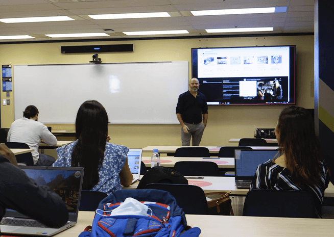 Étudiants universitaires avec des ordinateurs portables dans un amphithéâtre, concentrés sur un professeur près d'un écran de présentation.