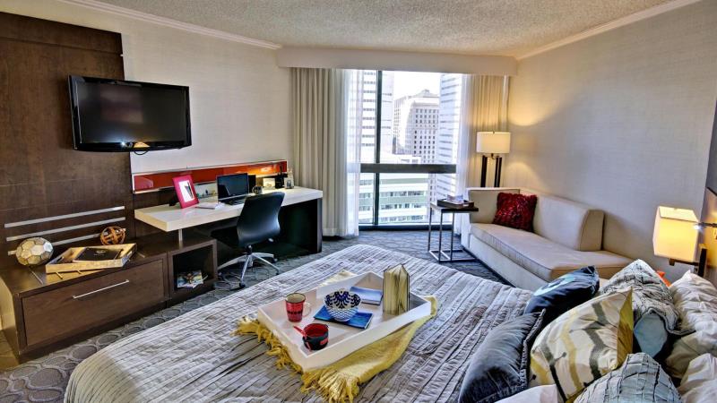 Une chambre d'hôtel confortable avec un bureau, un lit douillet et un coin salon, tous avec vue sur la ligne d'horizon de la ville.