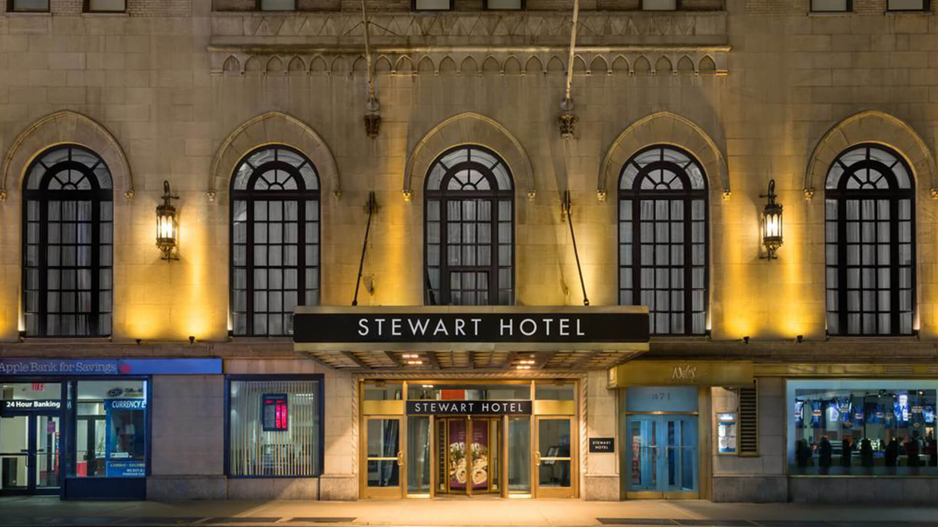 The Stewart Hotel's entrance illuminated by warm lights at night, showcasing its elegant architecture and welcoming atmosphere.