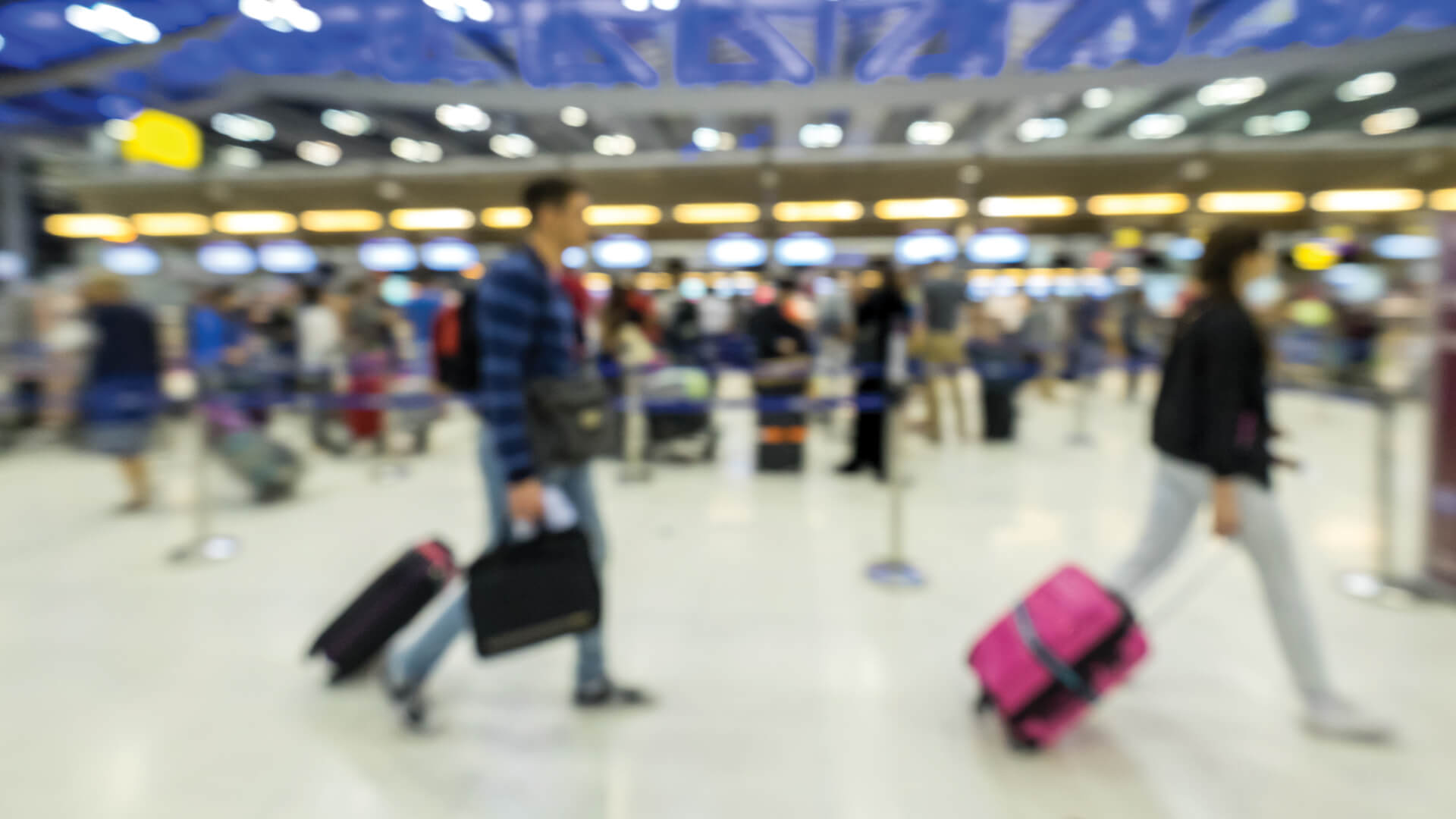 Image floue de passagers avec bagages dans un terminal d'aéroport animé, saisissant l'agitation du voyage.
