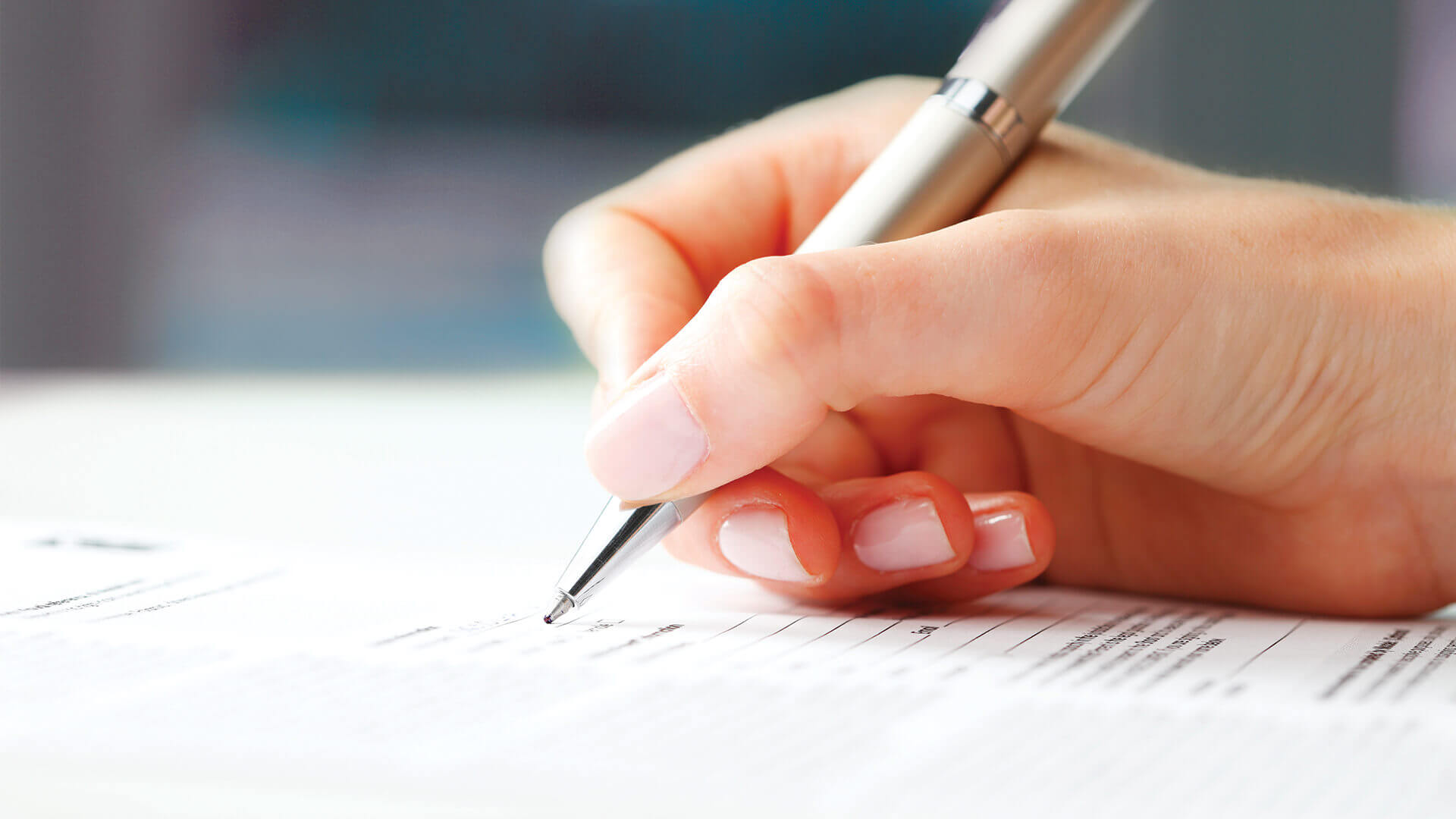 A close-up of a person's hand holding a pen and signing a document, emphasizing attention to detail.