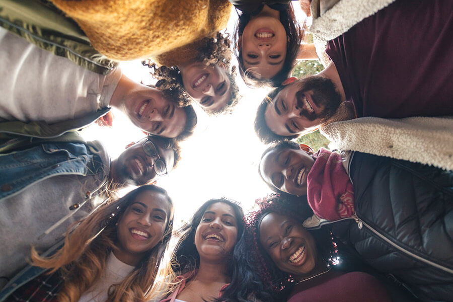 A diverse group of friends forming a circle, smiling directly above the camera.