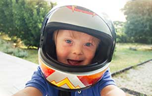 A beaming baby with blue eyes wearing an oversized motorcycle helmet, exuding happiness and playfulness.