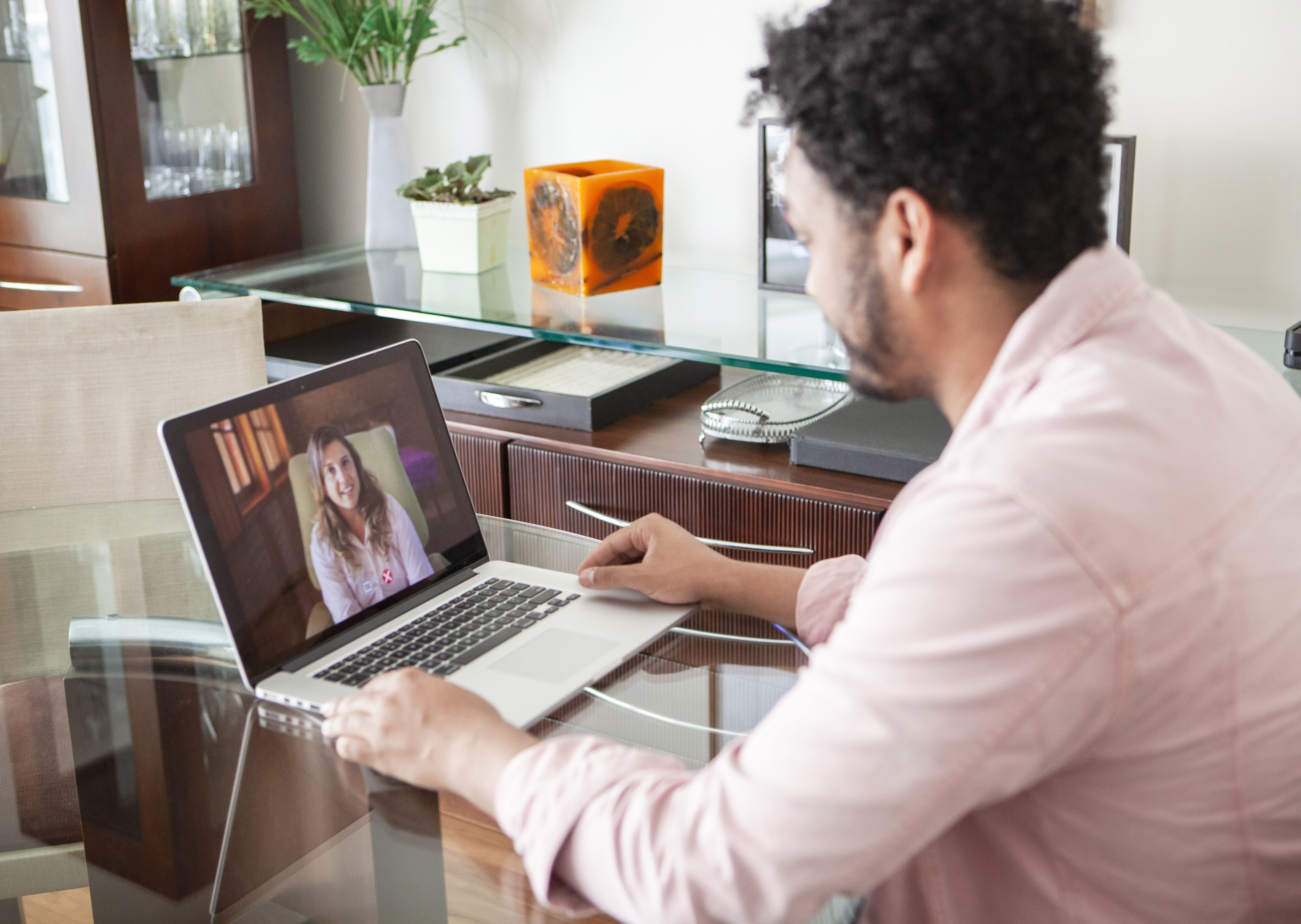 Un homme en chemise rose participe attentivement à un appel vidéo sur son ordinateur portable à domicile.