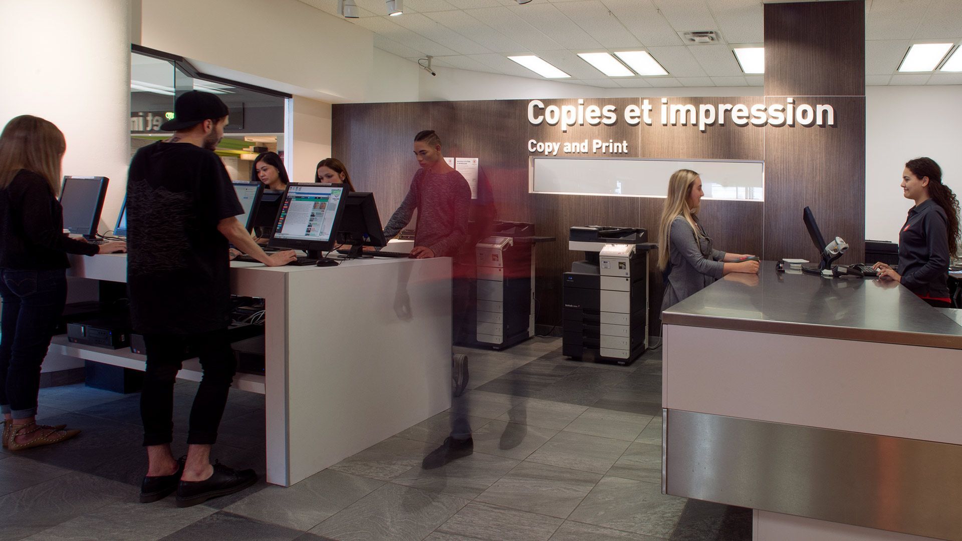 Customers and staff at a modern print service center with computers and copy machines.