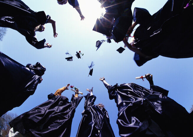 Graduates tossing their caps into the air, captured from a low angle against a clear sky, conveying a sense of achievement and joy.