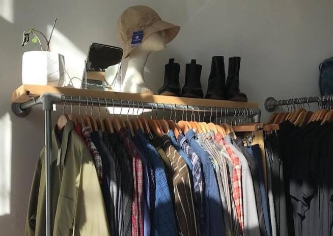 A neatly arranged wardrobe with a variety of shirts on hangers, flanked by boots and a hat on the shelf above.