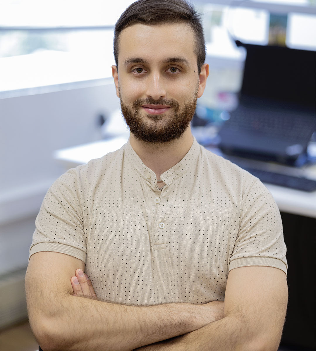 A well-groomed man with a beard, arms crossed, exuding confidence in a modern office environment.
