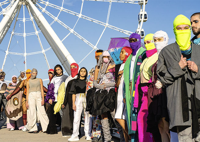 Un rassemblement multiculturel de personnes en tenues colorées devant une grande roue, symbolisant l'unité et la diversité.