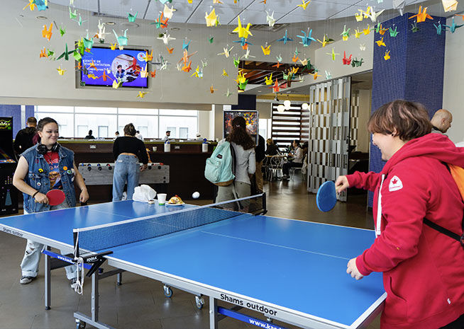 Des personnes profitant d'une partie de ping pong dans un cadre intérieur décontracté avec des décorations en origami au plafond.