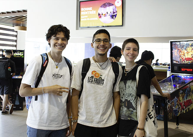 Trois amis souriant et posant pour une photo dans une salle d'arcade, avec des jeux en arrière-plan.