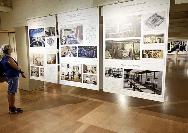 Un individu observe une exposition de projets d'architecture et de design d'intérieur, mettant en avant l'innovation et le style.