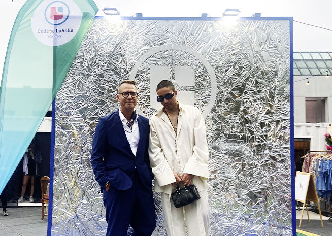 Two fashion figures stand before a striking foil backdrop, exuding style at a fashion event.