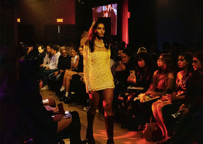 Un mannequin présente élégamment une robe jaune sur le podium, entouré par un public plongé dans l'expérience de la mode.