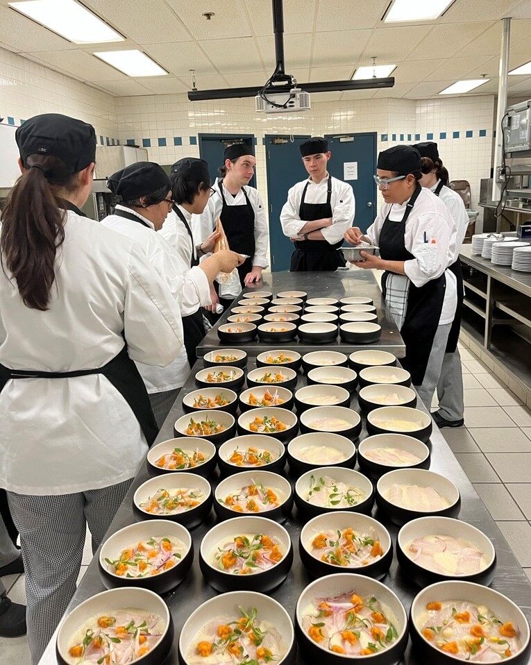Chefs in white uniforms are meticulously garnishing soup dishes in a professional kitchen, coordinating their efforts for service.
