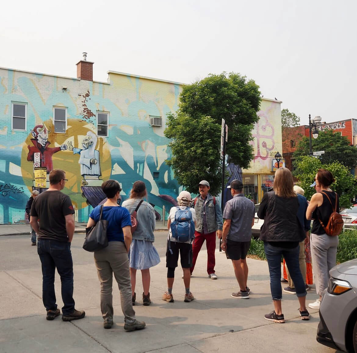 A group of people attentively listens to a guide while exploring vibrant street murals in an urban setting.