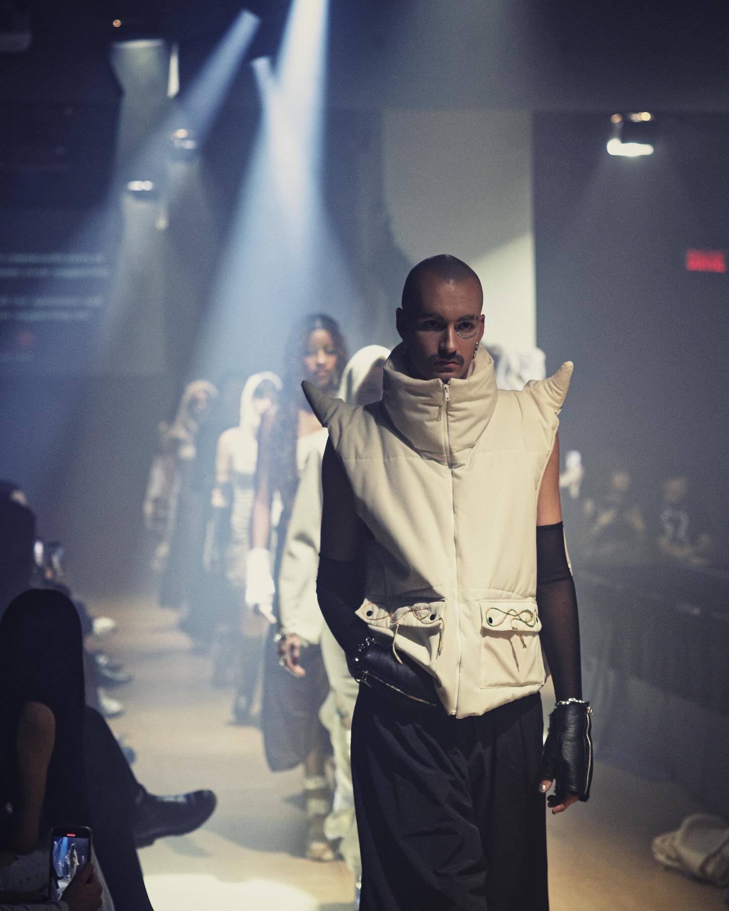 Un mannequin défile dans une tenue sculpturale innovante lors d'un défilé de mode, mettant en lumière un design futuriste sous un éclairage dramatique.