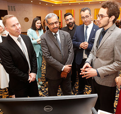 Un groupe de professionnels écoute attentivement une présentation lors d'un événement de réseautage, avec un écran d'ordinateur au premier plan.

