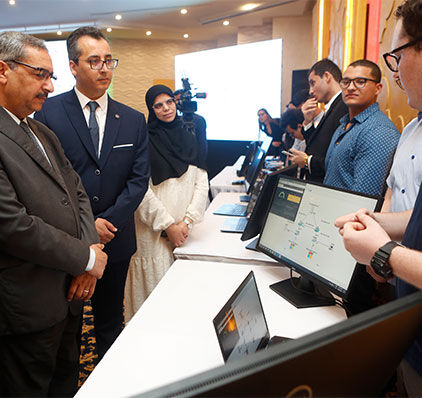 Les participants interagissent avec un présentateur qui réalise une démonstration technologique sur des tablettes lors d'un événement professionnel.