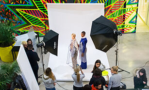 Behind-the-scenes view of a fashion photoshoot with models, photographers, and lighting equipment in a vibrant studio setting.