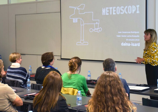 A speaker engages with an attentive audience during a meteorological presentation titled 'METEOSCOPI'.