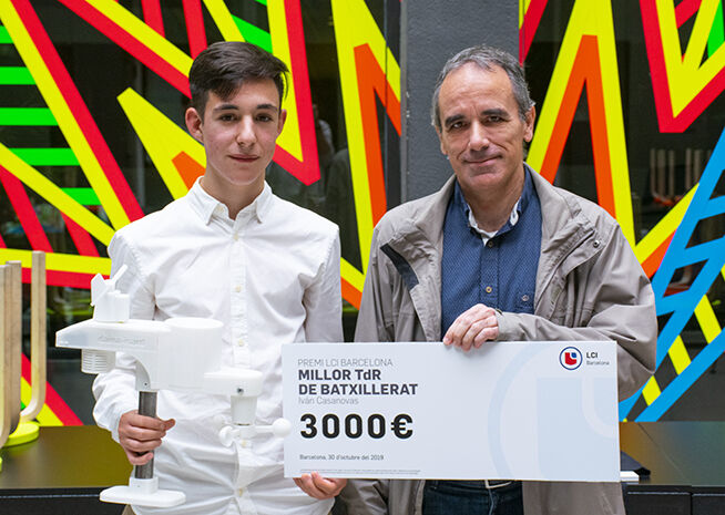 Un jove i un home més gran posen amb un xec de celebració de 3000€, atorgat per la 'Millor Tesi de Batxillerat' a Barcelona, datat d'octubre de 2019.
