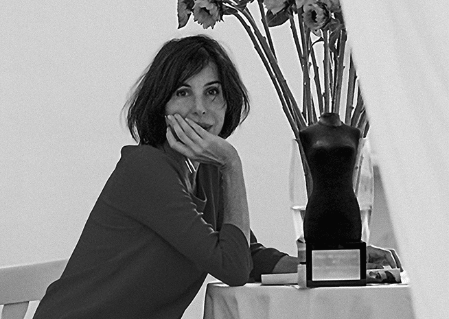 A woman poses thoughtfully beside an award sculpture and flowers, captured in a serene monochrome setting.