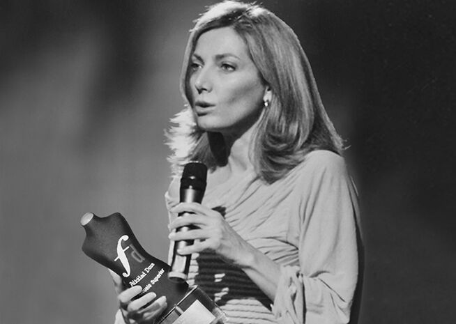 Una dona fa un discurs amb un premi a les mans, capturada en una fotografia en blanc i negre.