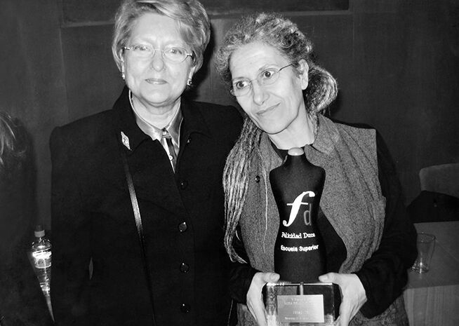 Dues dones posant amb un premi, una amb una placa, en una fotografia en blanc i negre.