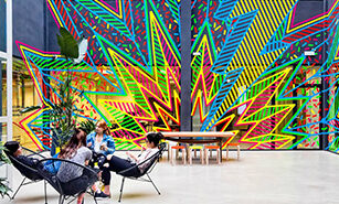 A lively communal space with people relaxing amidst bold geometric murals.