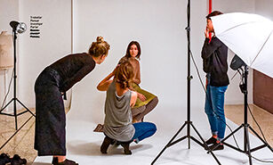 Behind-the-scenes view of a photo shoot with a photographer, model, and stylist working under studio lighting.